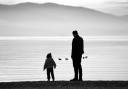 A father and child on the banks of a loch. Credit: Canva