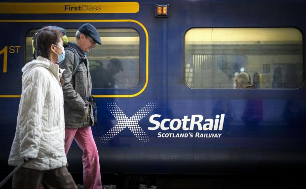 Clydebank Post: Two people walking in front of a Scotrail train. Credit: PA